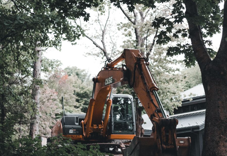 Excavator parked beside a wooded Asheville house during drain field work